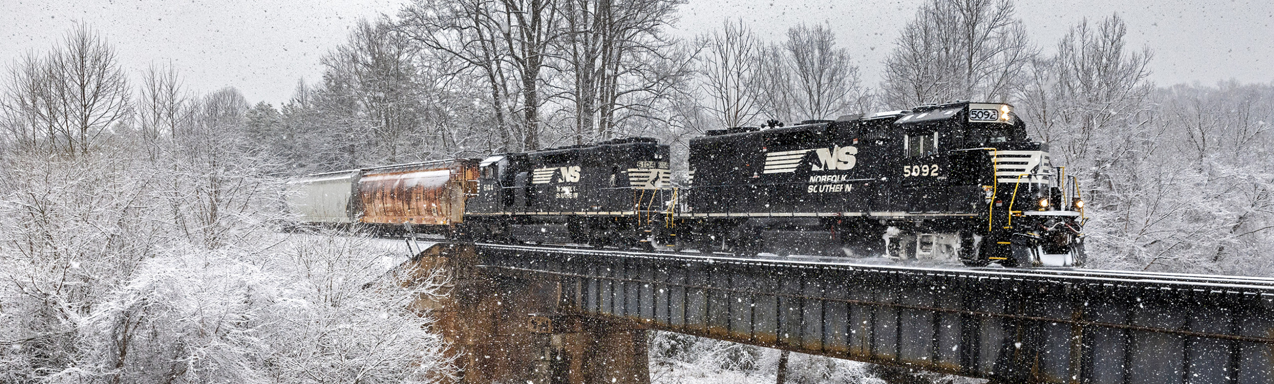 Photo of a black Norfolk Southern locomotive on a bridge in snowy  weather shot by photographer Trey Belton